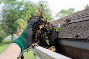 gloved hand pulling out dirt from gutters