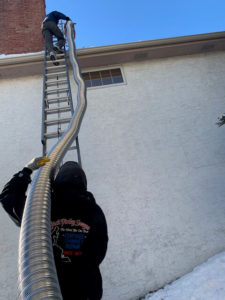 Two technicians pulling a long stainless steel chimney liner up a ladder to the chimney